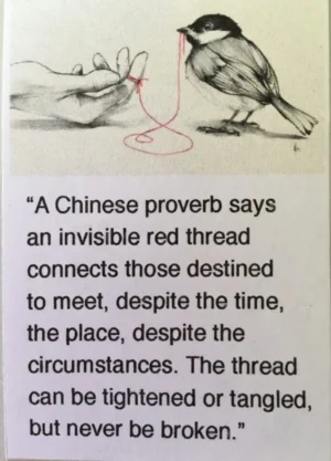 A bird holds a red string in its beak while the other end ties to a human's pinky finger.